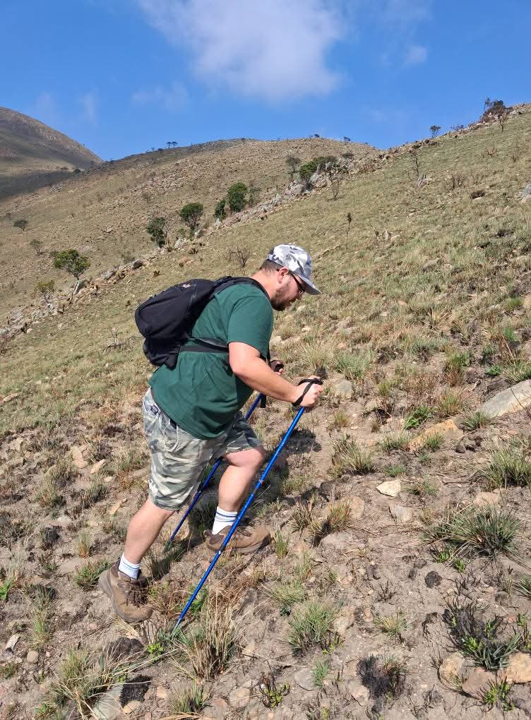 Hiker ascending a grassy ridge of the Makhonjwa Mountains near Barberton under a clear blue sky